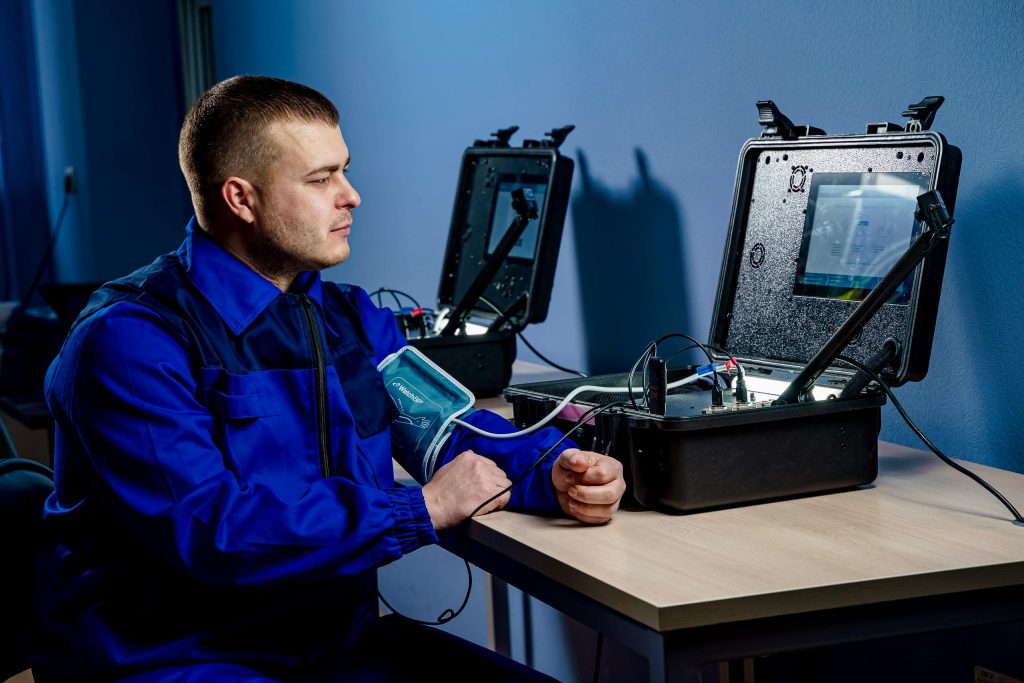 A man in a blue uniform using advanced medical equipment for health monitoring indoors.